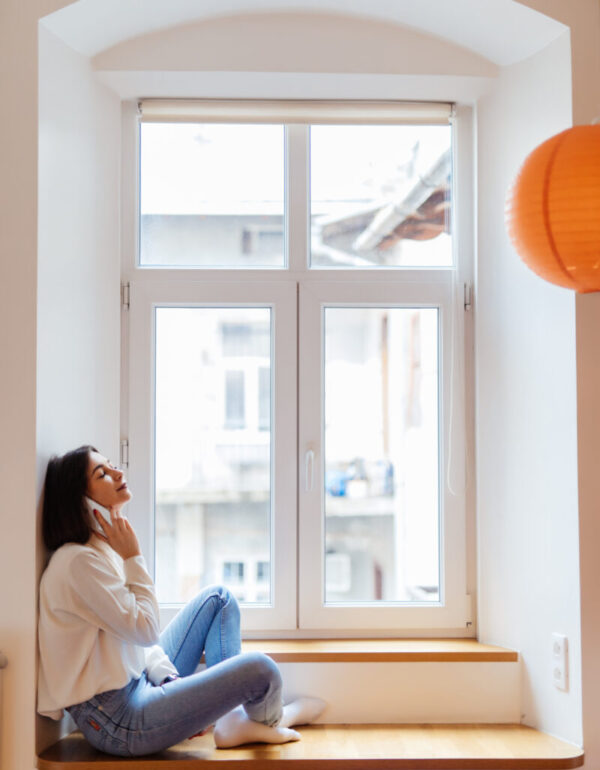 charming woman is talking on phone while sitting near the window