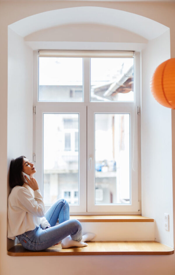charming woman is talking on phone while sitting near the window